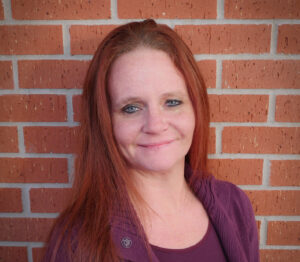 Woman smiling at the camera, standing in front of a brick wall