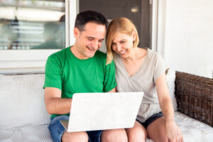 Middle aged couple looking a laptop, smiling, and pointing. They are sitting on a couch